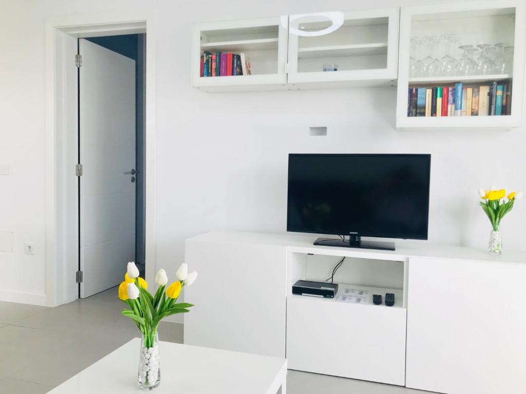 a white living room with a tv and flowers on a table at Apartamento Los Mangos 34 in Maspalomas
