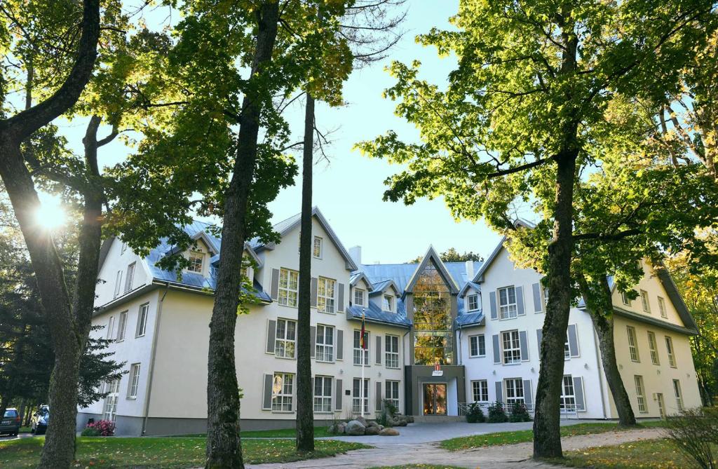 een groot wit gebouw met bomen op de voorgrond bij Sanatorija ,,Tulpės" in Birštonas