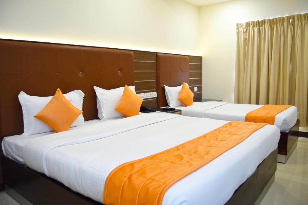 2 letti in camera d'albergo con cuscini arancioni di Thiviyam Airport Hotel a Chennai