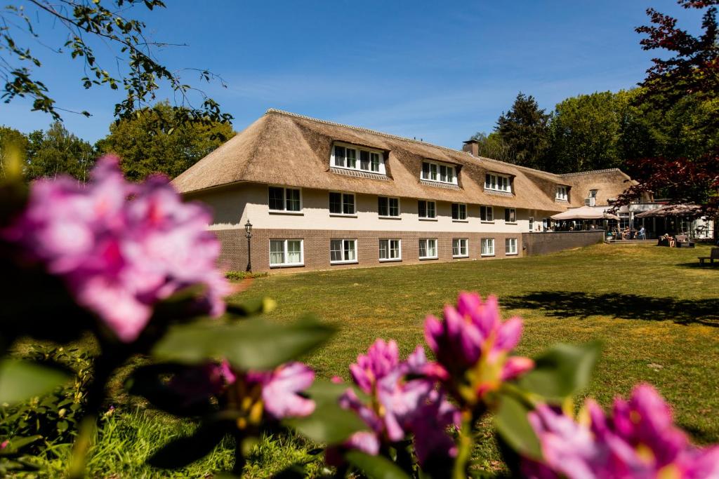 ein großes Gebäude mit einem Rasenhof mit rosa Blumen in der Unterkunft Landhuis Hotel de Herikerberg in Markelo