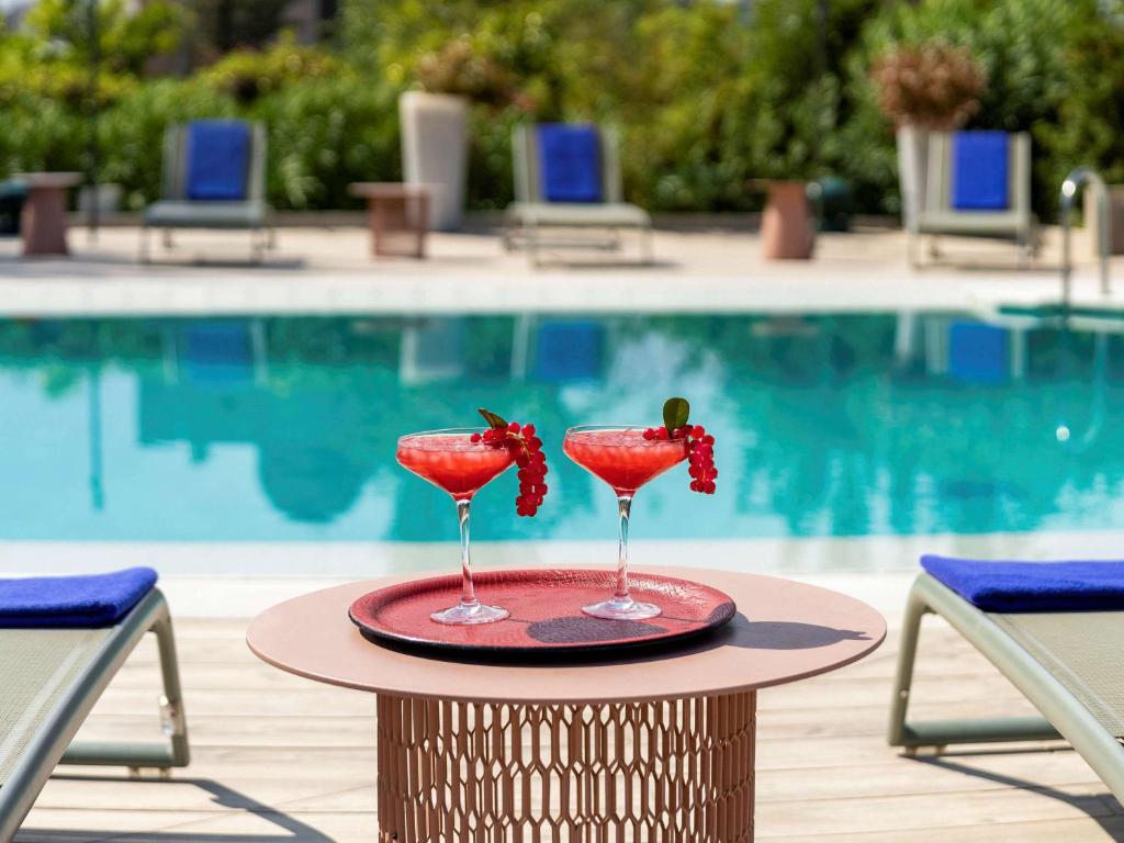 deux verres à vin avec des raisins sur une table à côté d'une piscine dans l'établissement Ibis Styles Madrid City Las Ventas, à Madrid