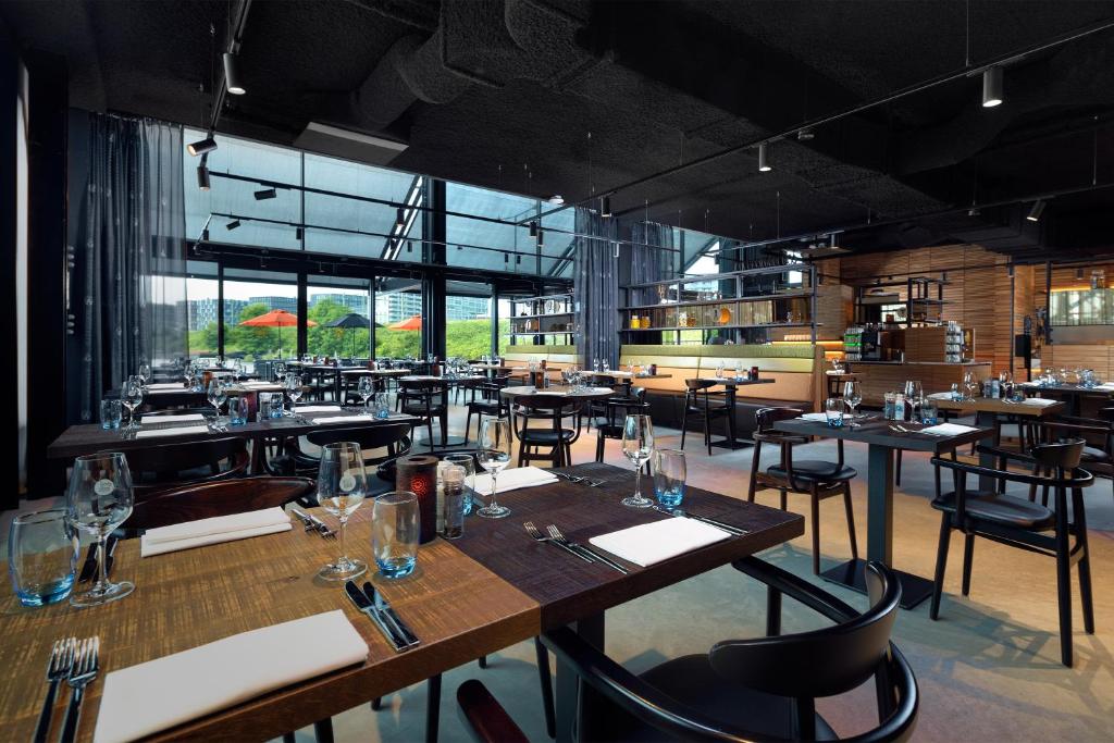 een restaurant met houten tafels, stoelen en ramen bij Inntel Hotels Amsterdam Landmark in Amsterdam