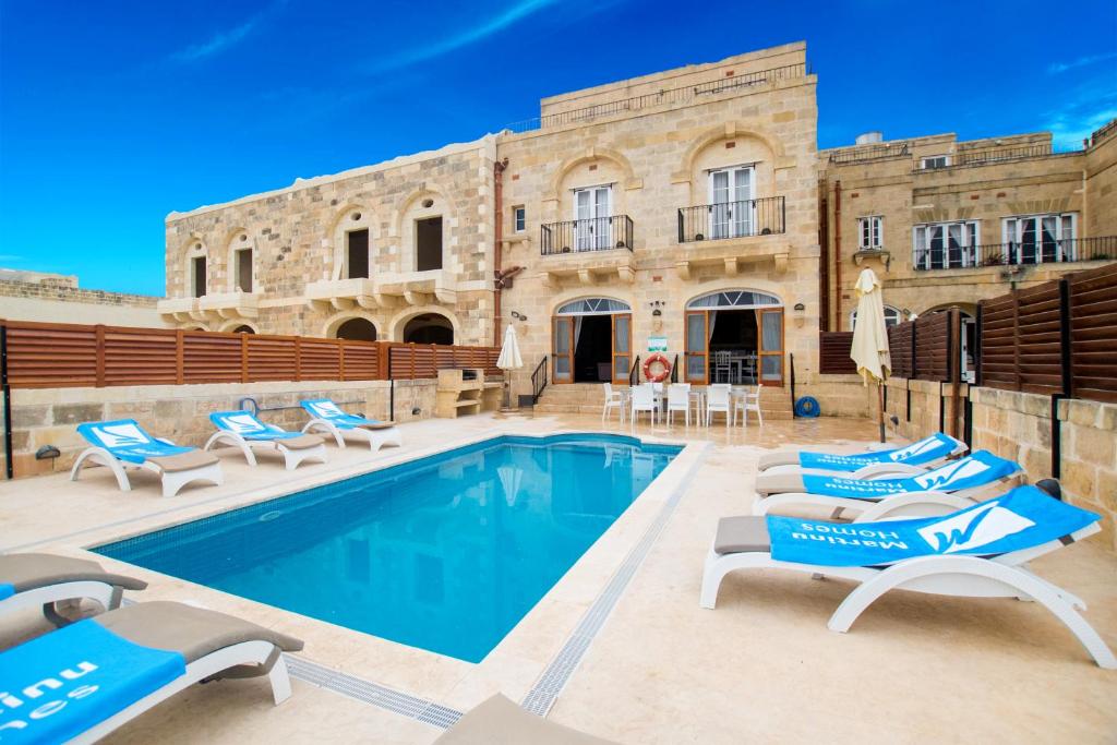 a swimming pool with lounge chairs and a building at Ta' Peppi in Sannat
