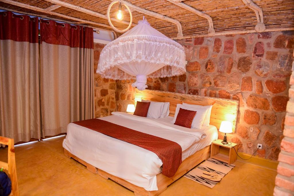 1 dormitorio con 1 cama grande en una pared de piedra en Akagera Transit Lodge en Akagera