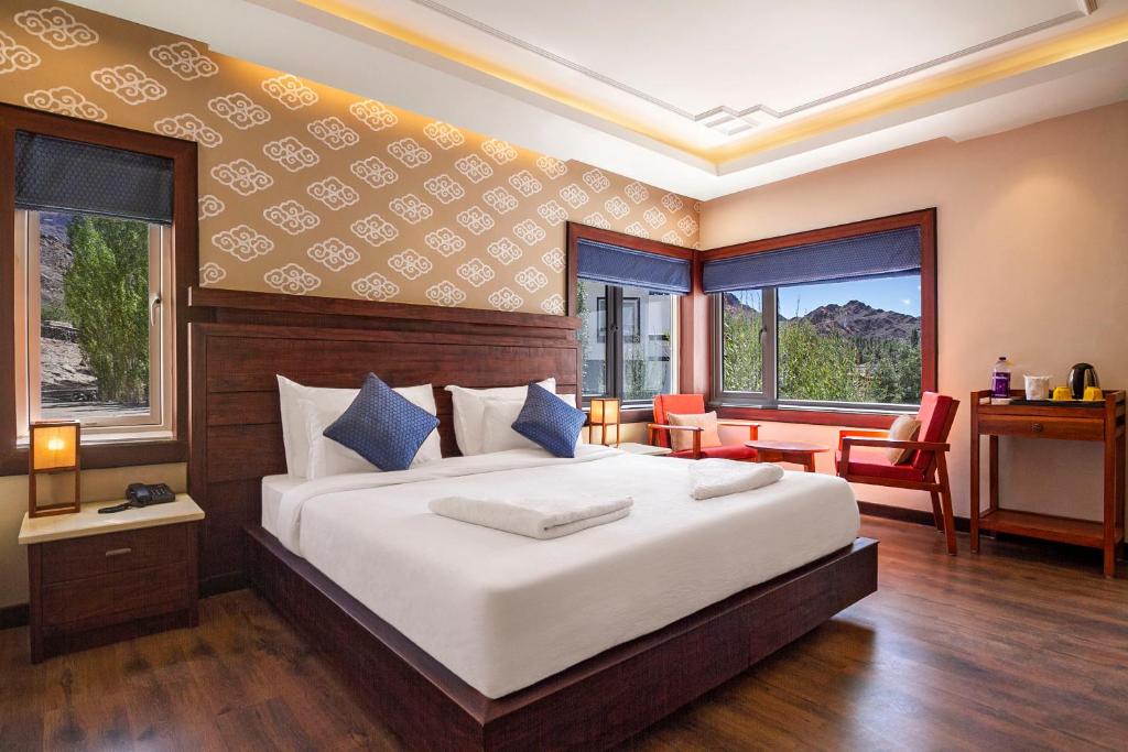 a bedroom with a bed and a desk and two windows at ANGKASA LADAKH RESORT in Leh