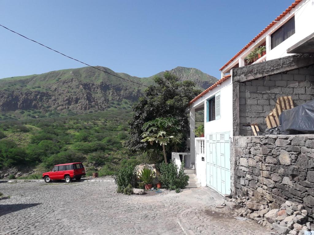 een rode auto geparkeerd naast een huis met een berg bij Ponta Gato Residence in Tarrafal