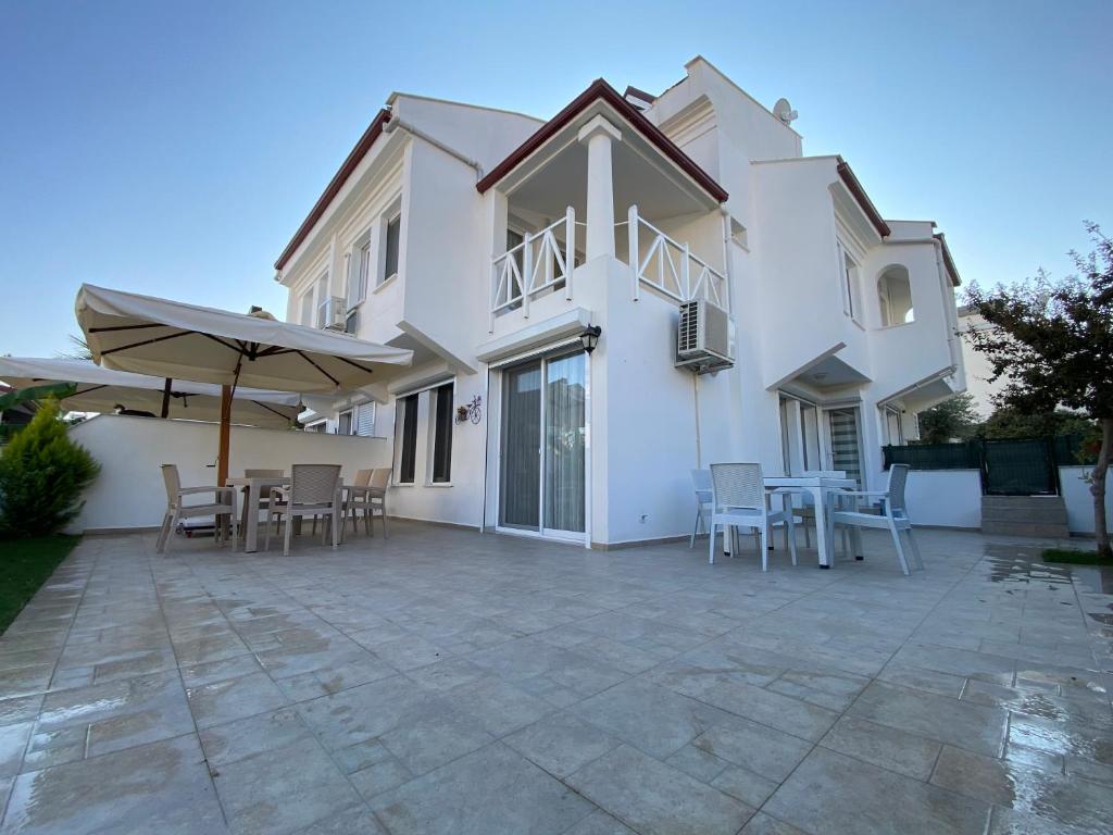 a white house with a patio with chairs and an umbrella at The Family Villa in Kuşadası