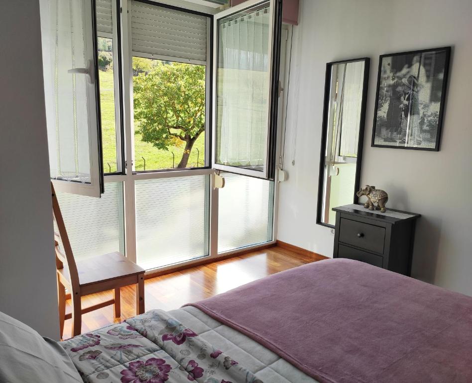 a bedroom with a bed and a chair and windows at APARTAMENTO VALMAYOR in Potes