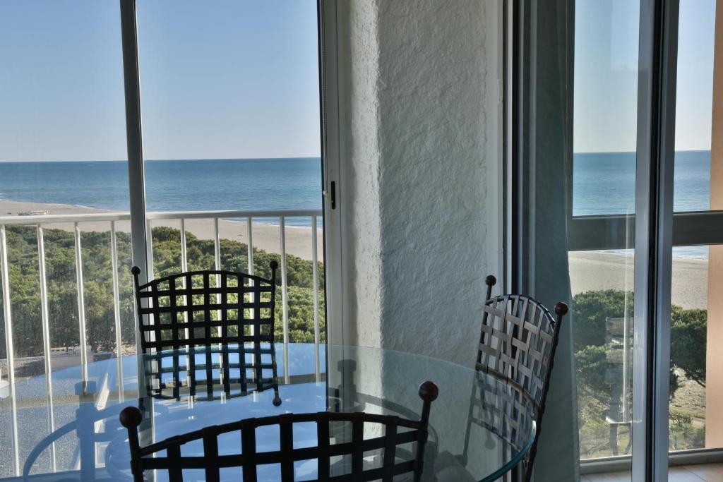 uma sala de jantar com uma mesa de vidro e cadeiras e o oceano em Le Belvédère - T2 en front de mer em Argelès-sur-Mer