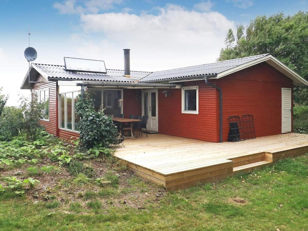 ein kleines rotes Haus mit einer Holzterrasse in der Unterkunft 6 person holiday home in Thyholm in Thyholm