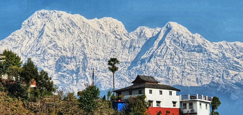 a snow covered mountain with a house in front of it at Club ES Deurali Resort in Pokhara