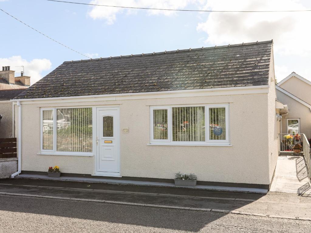 a white house with a white door on a street at Bwthyn Tyn y Coed in Bryngwran