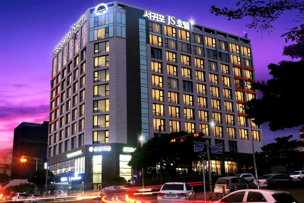 a tall building with cars parked in front of it at Seogwipo JS Hotel in Seogwipo