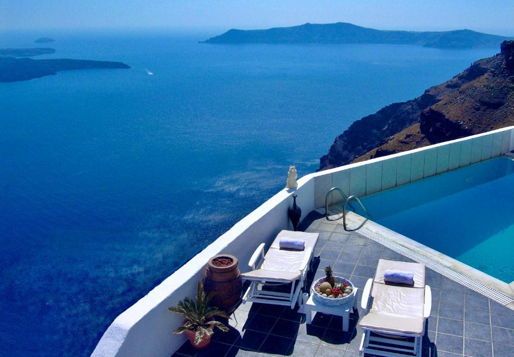 una piscina con 2 sillas y el océano en Aeolos Art & Eco Suites Adults Only en Imerovigli