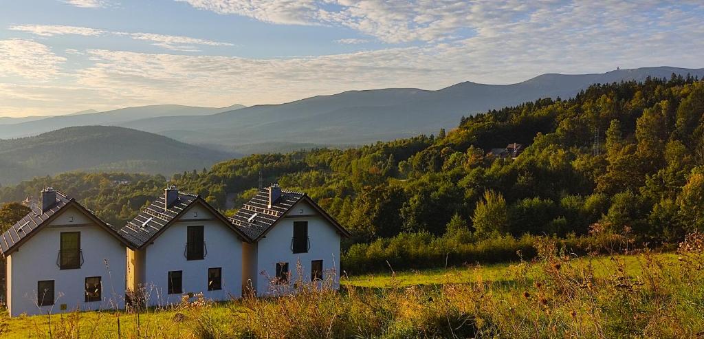 duas casas brancas numa colina com montanhas ao fundo em Domki Na Skale z widokiem na panoramę Karkonoszy em Szklarska Poręba