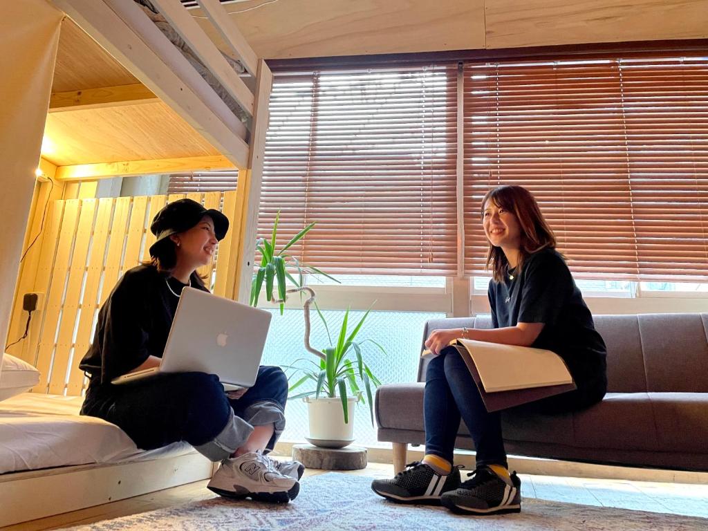 two women sitting on a couch with a laptop at Hostel Ini kobe & Donut cafe in Kobe