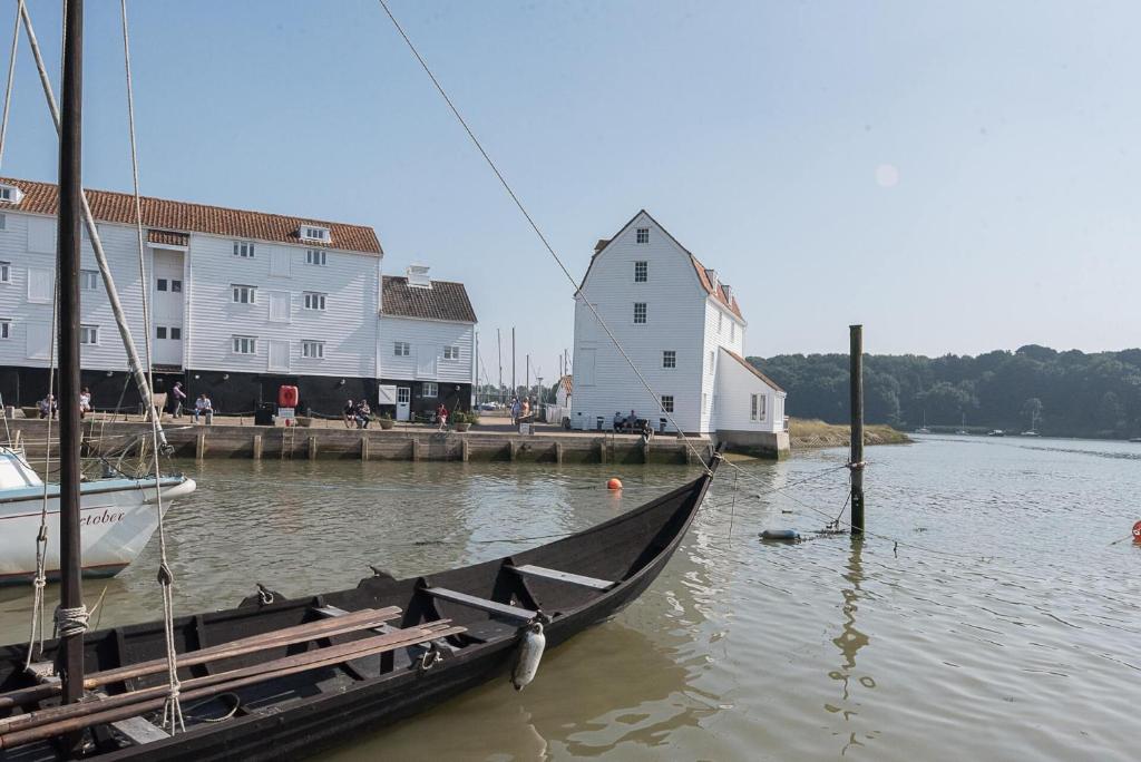 伍德布里奇的住宿－The Old Granary Cottage Woodbridge Air Manage Suffolk，船停靠在水中,靠近一座建筑