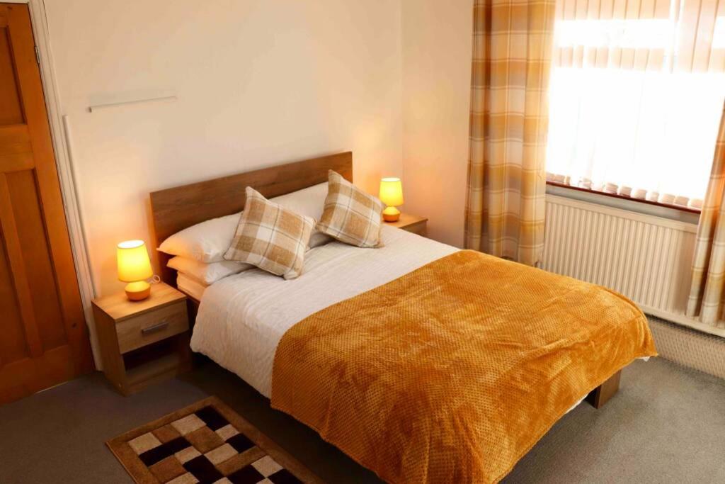 a bedroom with a bed with two lamps and a window at Cheerful 2 bedroom residential home - Free parking in Leeds