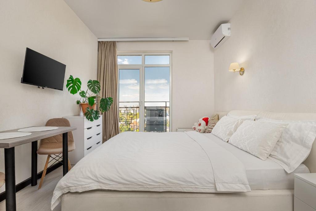 New apartments in Arcadia sea view في أوديسا: غرفة نوم بيضاء بها سرير ومكتب ونافذة