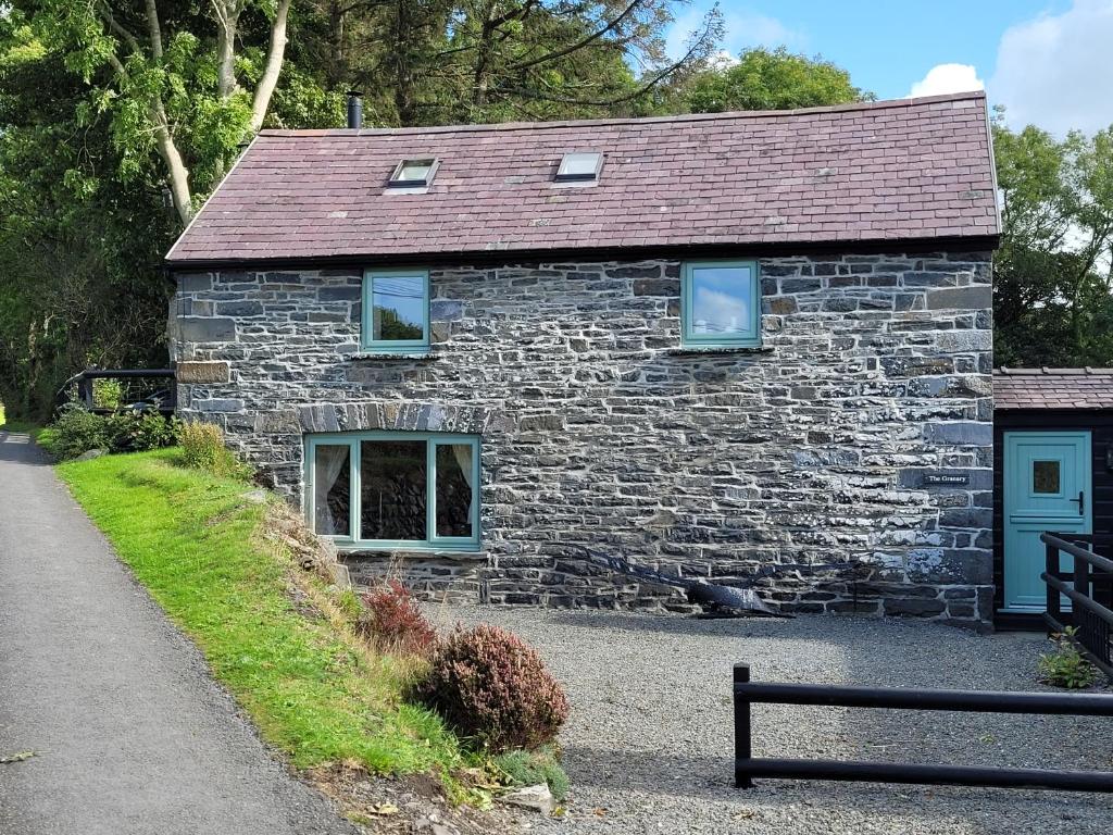 une maison en pierre avec des fenêtres bleues et un banc dans l'établissement The Granary, à Llanddeiniol