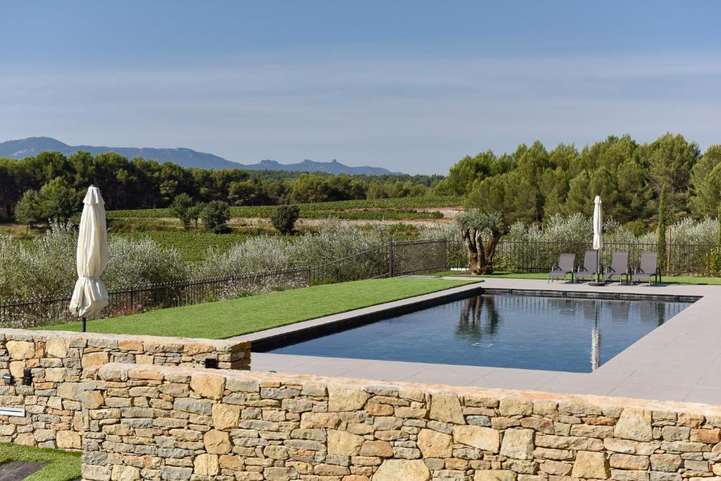 a swimming pool with a stone wall and an umbrella at Domaine de la Galinière in Châteauneuf-le-Rouge