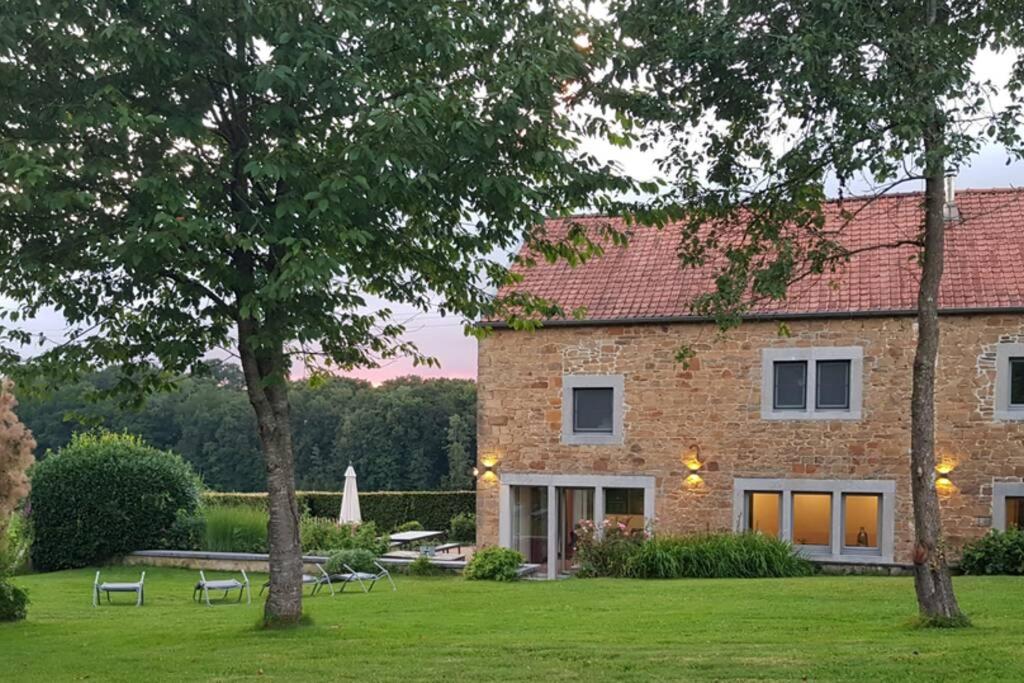 une grande maison en briques avec une pelouse et des arbres dans l'établissement Gite rural '21 bonnes raisons' - Ossogne, à Havelange