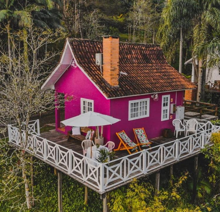 a pink house with chairs and an umbrella at Pousada Vale Dos Figos in Urussanga
