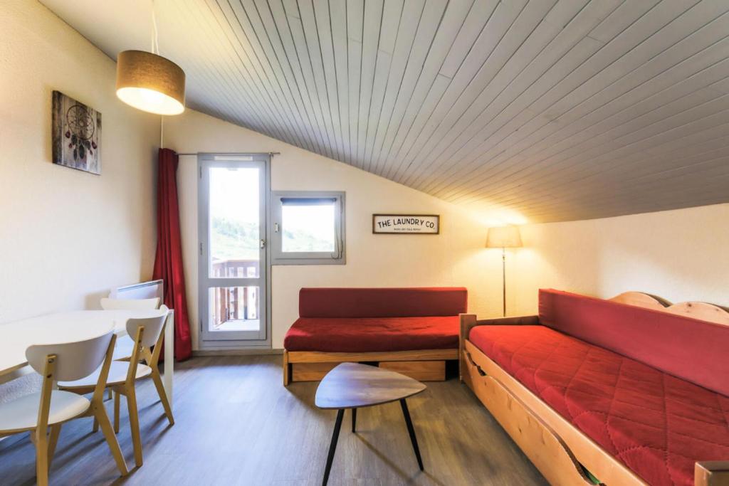 1 dormitorio con cama roja, mesa, mesa y sillas en Résidence Pierre de Soleil - maeva Home 77590, en Aime La Plagne