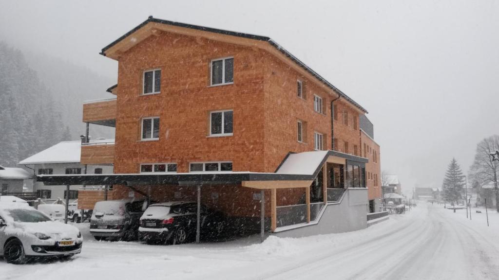 un gran edificio de ladrillo en la nieve con coches aparcados en Alpine Lodge Klösterle am Arlberg, en Klösterle am Arlberg