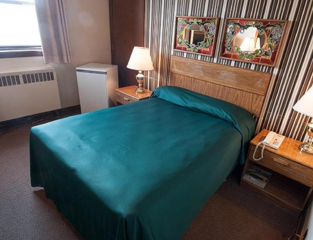 una camera d'albergo con un letto con una coperta blu di Curtis Gordon Motor Hotel a Winnipeg
