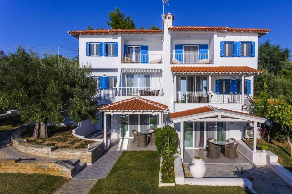une grande maison blanche avec des fenêtres bleues et une cour dans l'établissement Holiday residence Acrotel Athena Villas, Elia Beach, à Kalogria
