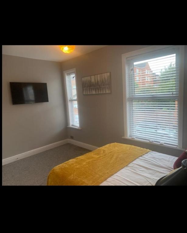 a bedroom with a bed and a tv and two windows at Beautiful stylish house near town centre in Rugby