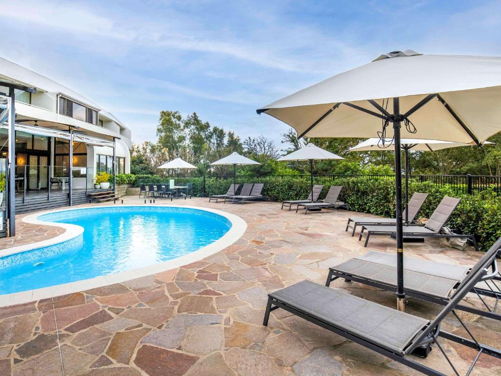 a swimming pool with chairs and an umbrella at Mercure Charlestown in Newcastle