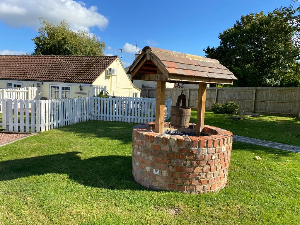a brick fountain in a yard with a white fence at fairfeilds cottage Frog Trotters Bottom in Hartpury