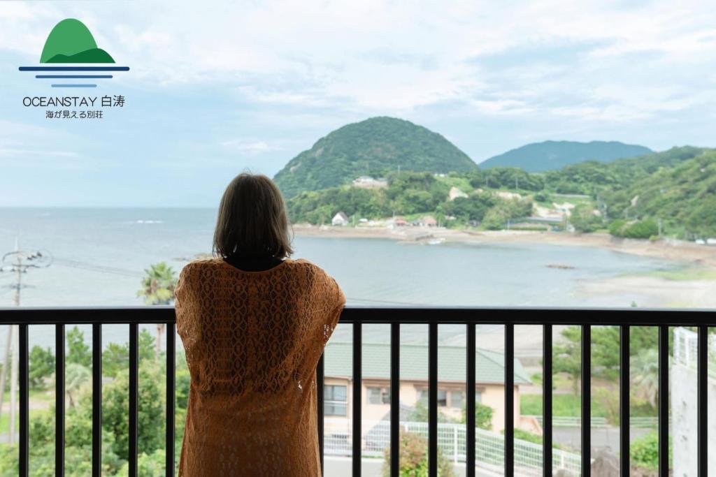 Eine Frau steht auf einem Balkon mit Meerblick in der Unterkunft OCEANSTAY SHIRATO - Vacation STAY 74540v in Iwaya