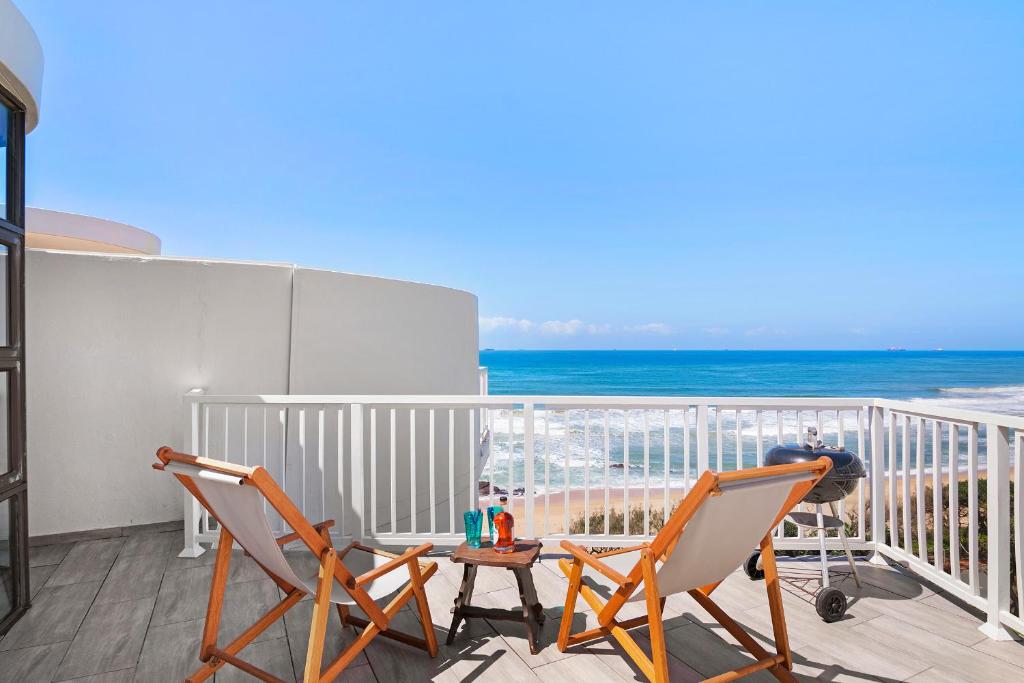 een balkon met 2 stoelen en een tafel en de oceaan bij Escape to a Coastal Oasis in Umdloti