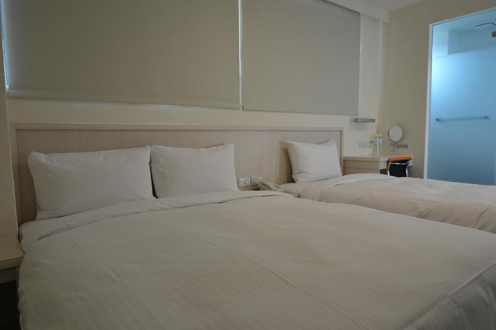 two beds in a hotel room with white sheets and pillows at Century Hotel in Kaohsiung