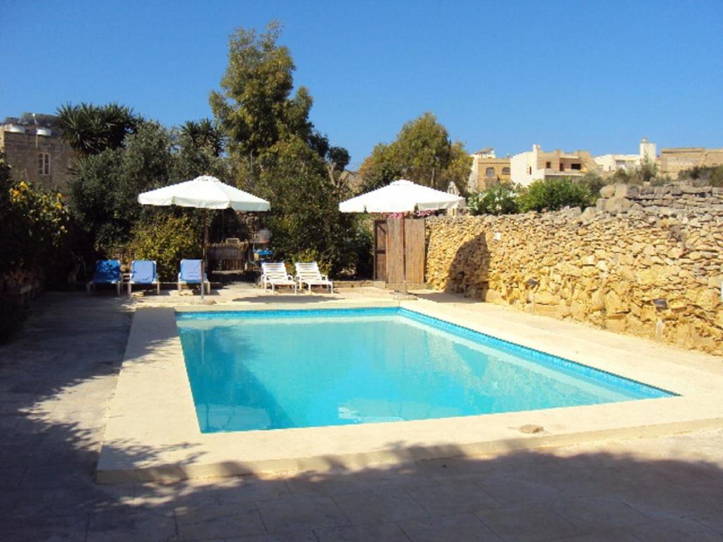 a swimming pool with two umbrellas and a stone wall at La Gozitaine in Kerċem