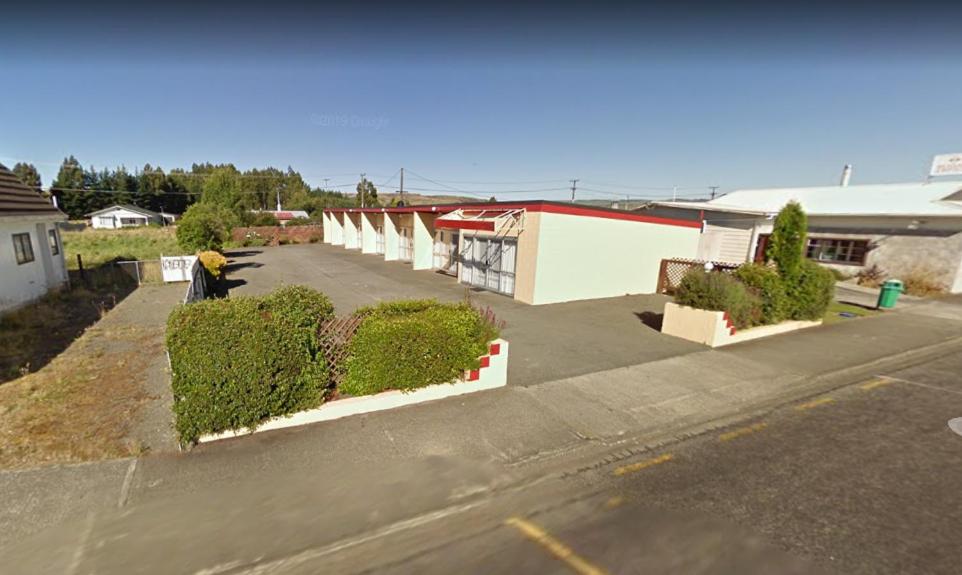un parking vide avec des buissons et un bâtiment dans l'établissement Roadside Motel, à Waiouru