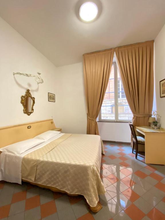 a bedroom with a bed and a desk and a window at Piccolo Hotel Etruria in Siena