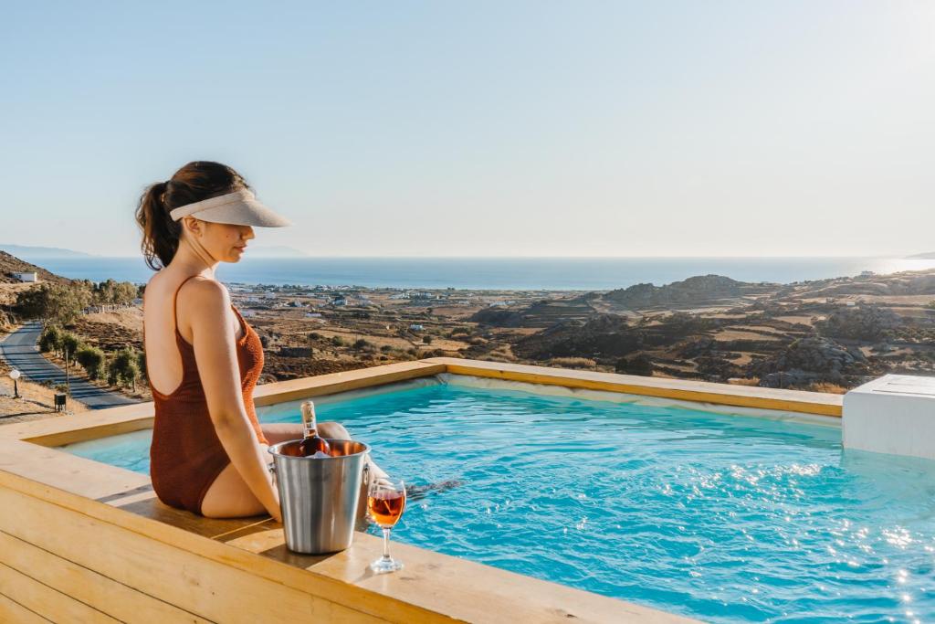 a woman sitting next to a swimming pool with a glass of wine at Naxos Aethereal View in Kastraki Naxou