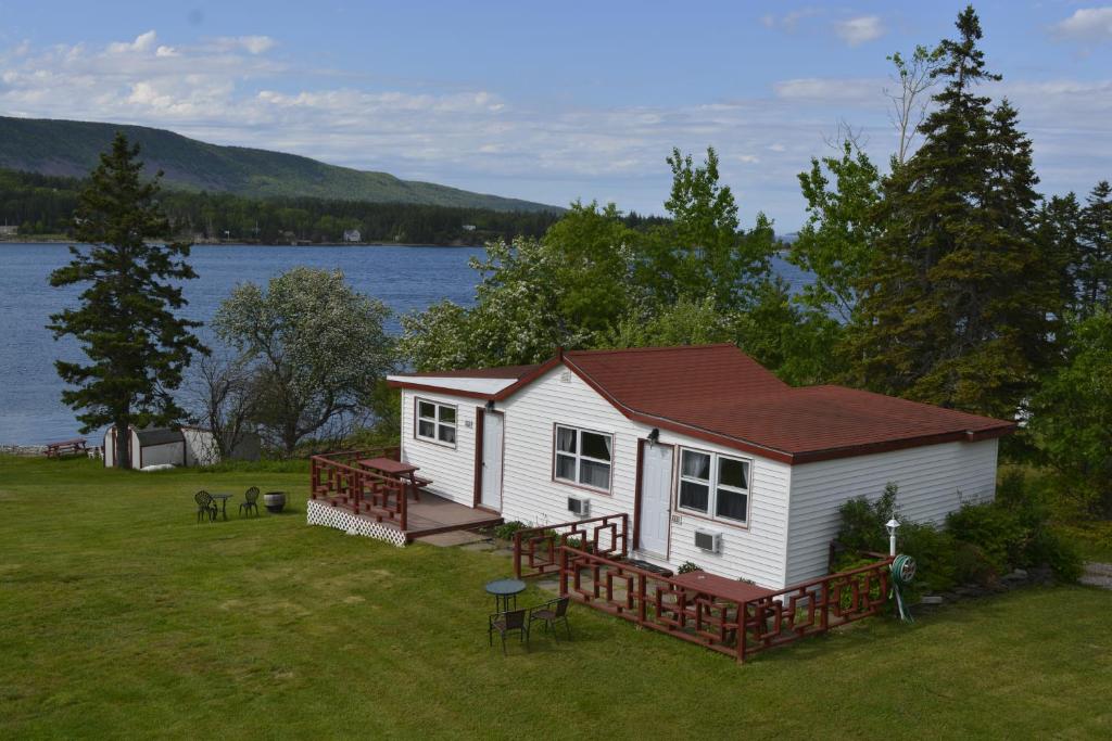 una pequeña casa blanca con una gran terraza junto al agua en Mountain Vista Seaside Cottages, en Big Bras d'Or