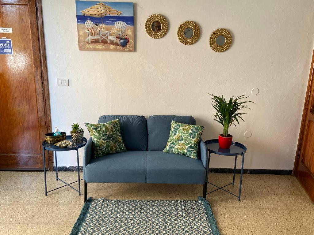 Sofá azul en una sala de estar con 2 mesas en Sarahs Kite Vivienda Vacacional en Playa del Burrero en Playa del Burrero