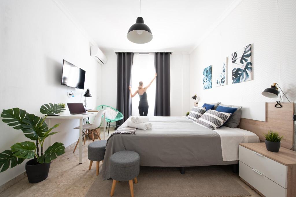 a bedroom with a bed and a desk and a woman out the window at Nordik Rooms Urban - Trinidad "Copenhague" in Málaga