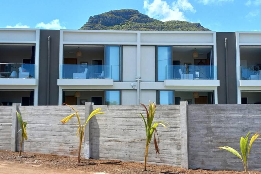 a building with a fence and palm trees in front of it at Bois Mapou Self Catering Apartments Unit 104 in Rivière Noire