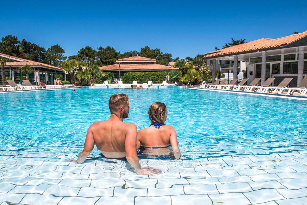 Ein Mann und eine Frau, die im Pool eines Resorts sitzen. in der Unterkunft Hôtel Les Grenettes in Sainte-Marie-de-Ré