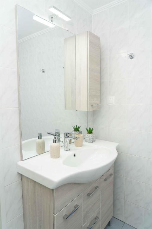 a white bathroom with a sink and a mirror at Tzortzi's Family Apartments in Kaloi Limenes