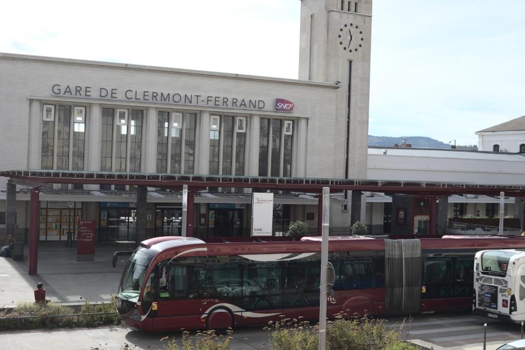 un bus rouge garé devant un immeuble doté d'une tour d'horloge dans l'établissement Le Petit Terminus - GARE SNCF, à Clermont-Ferrand