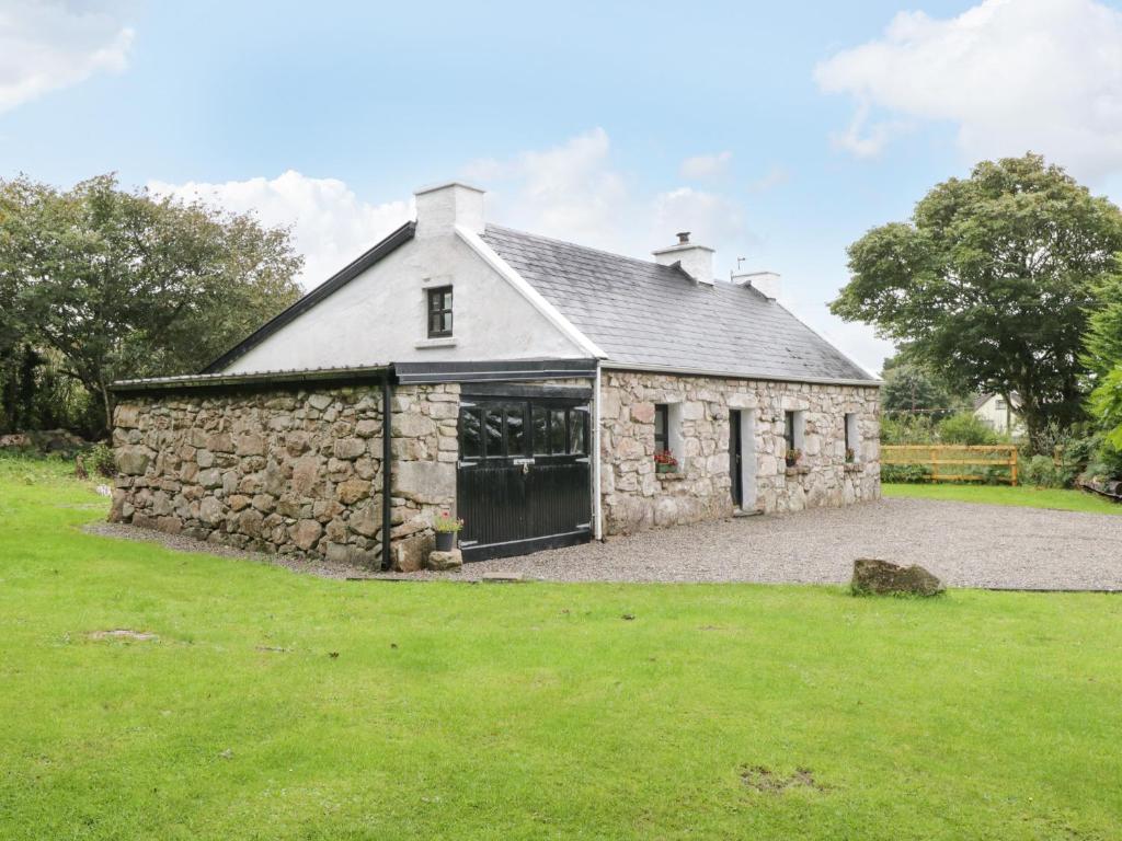 an old stone barn with a grass yard in front of it at An Teach Ban in Rossaveel