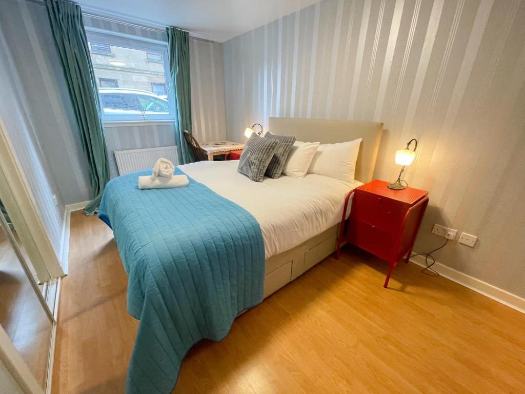 a bedroom with a bed with a blue blanket and a window at Kelvingrove 2 Bedroom Apartment - Private Parking in Glasgow